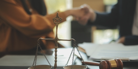 client and lawyer shaking hands in the background of scales and a gavel