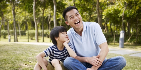 father and elementary-age son sitting on grass outdoors