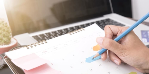Person holding pencil and writing on calendar.