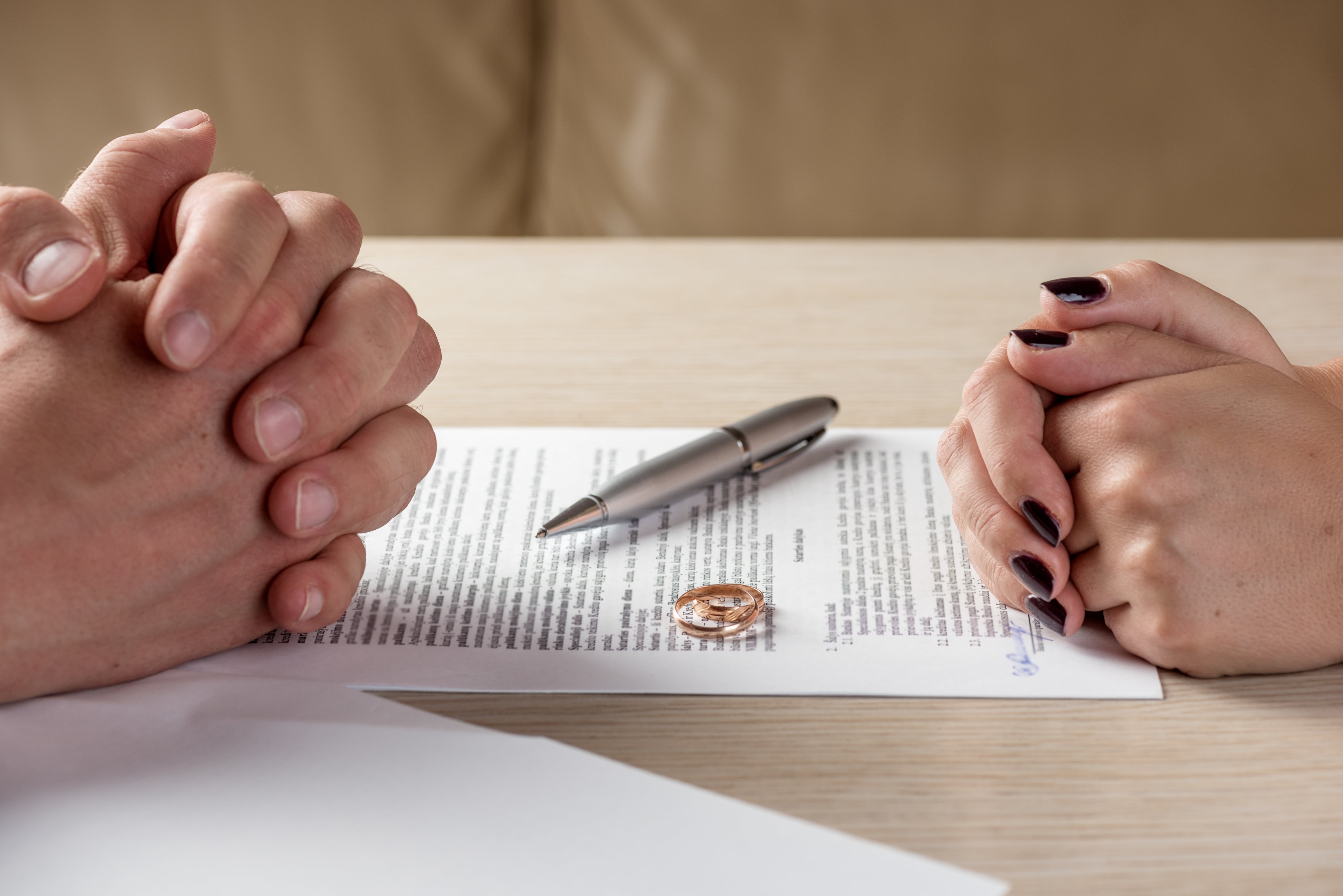 Divorce papers on a table with a couple's folded hands on either side of the table
