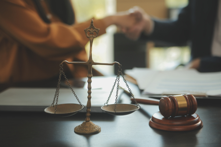 client and lawyer shaking hands in the background of scales and a gavel
