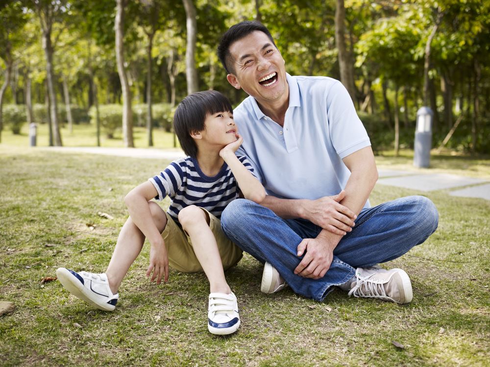 father and elementary-age son sitting on grass outdoors