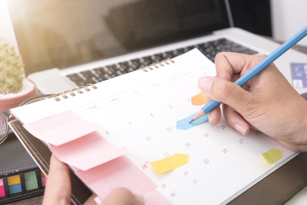 Person holding pencil and writing on calendar.
